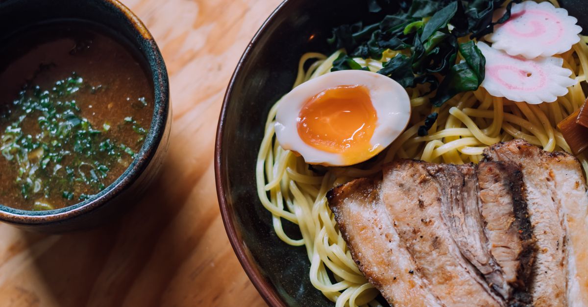 Schüssel Ramen mit Weizennudeln, weich gekochtem Ei, Chashu-Schweinefleisch und Narutomaki neben einer separaten Brühe