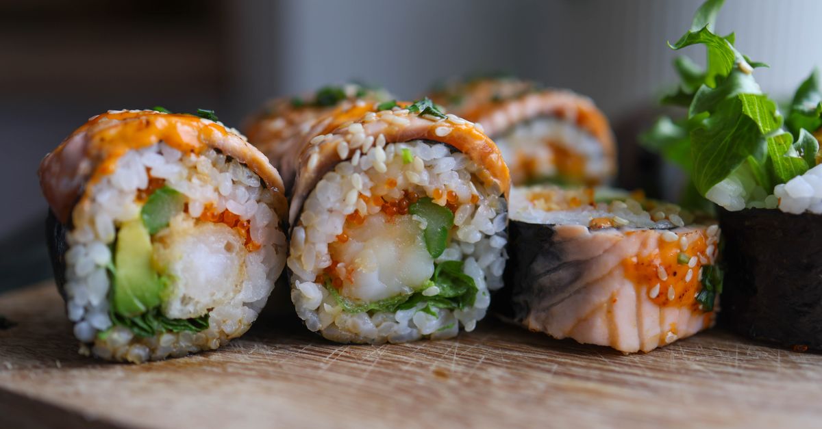 Frisch gerollte Sushi-Stücke mit Lachs, Avocado und Sesam auf einem Holzbrett