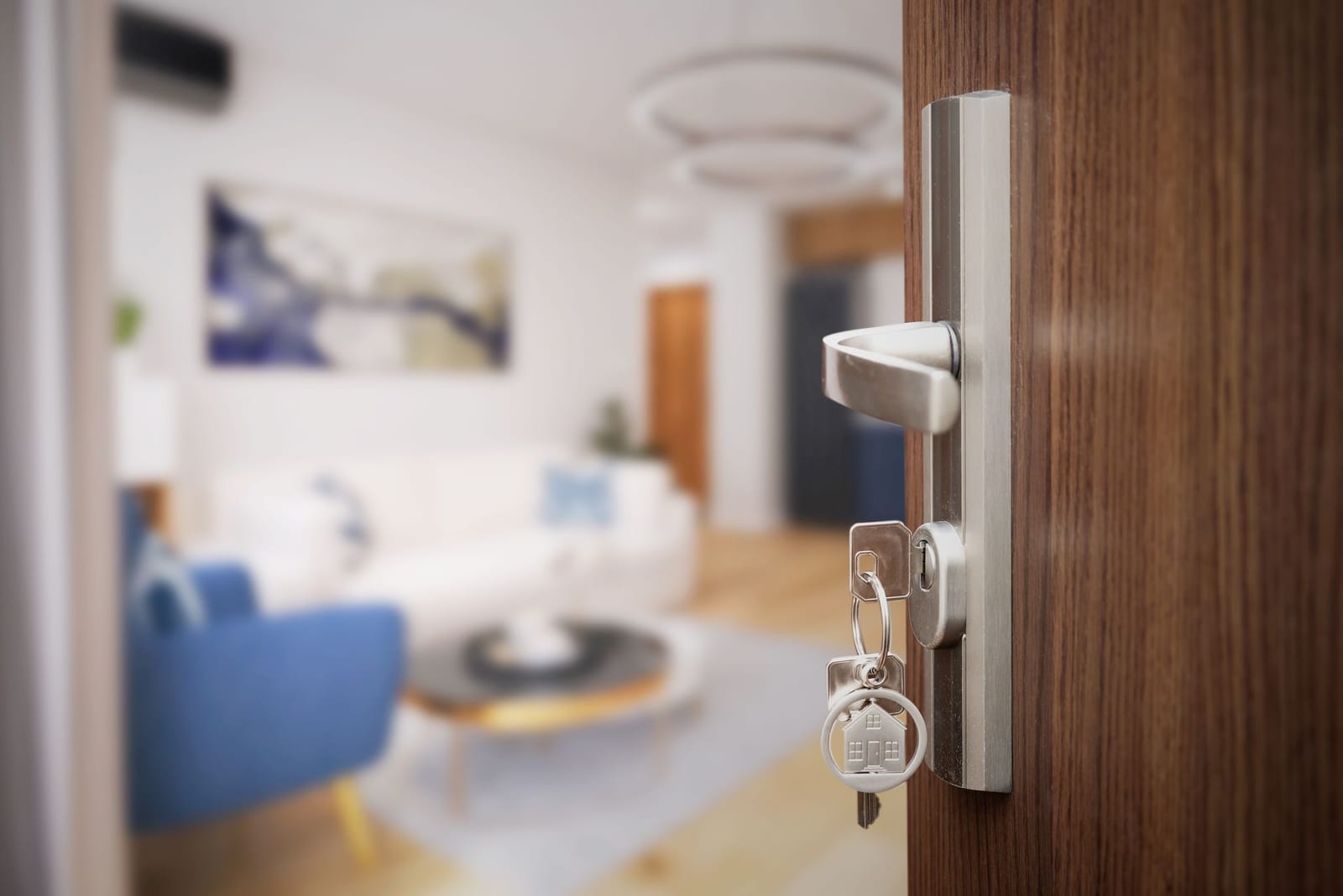Geöffnete Wohnungstür mit Schlüssel und Haus-Anhänger im Schloss, dahinter ein modern eingerichtetes Wohnzimmer