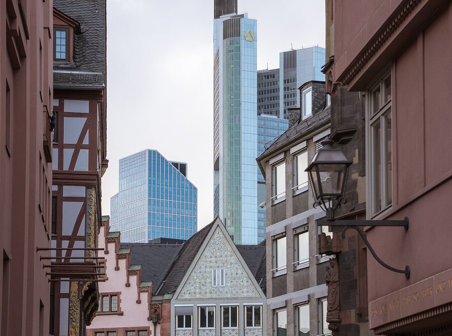 Eine schmale Straße in Frankfurt zeigt eine Mischung aus traditioneller und moderner Architektur. Fachwerkhäuser säumen den Vordergrund, während im Hintergrund elegante Wolkenkratzer, darunter der Commerzbank Tower, hervorstechen – eine perfekte Kulisse für Tipps zur Verwaltung von Eigentumswohnungen.