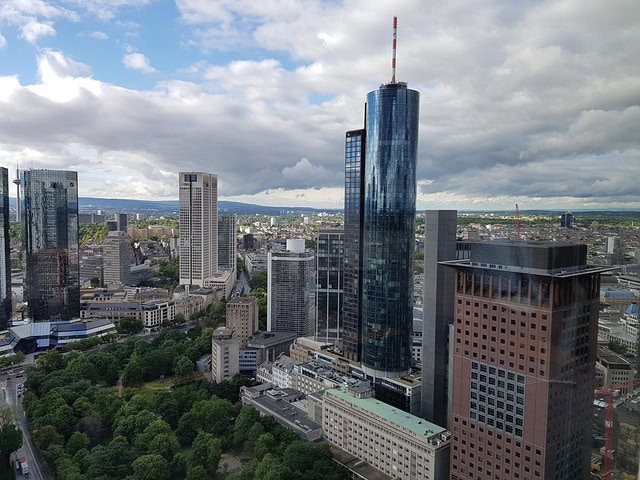 Ein Stadtbild in Frankfurt am Main: Moderne Wolkenkratzer und Glasbauten überragen einen großen Park mit grünen Bäumen, alles unter einem wolkenverhangenen Himmel - perfekt für alle, die Unterkünfte Bahnhofsnähe oder ein Hotel in der Innenstadt suchen.
